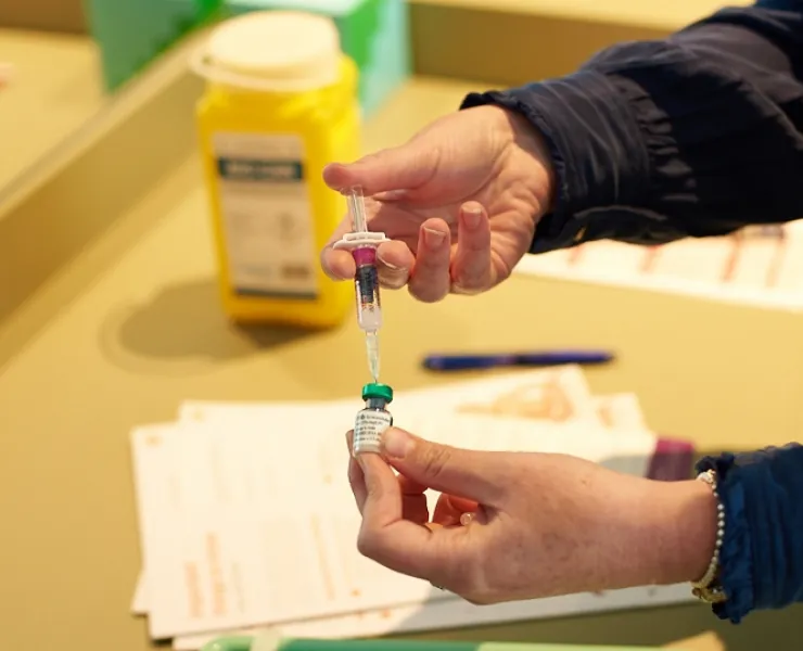 An immunisation nurse prepares a syringe from a vial of fluid. Only the nurse's hands are visible.